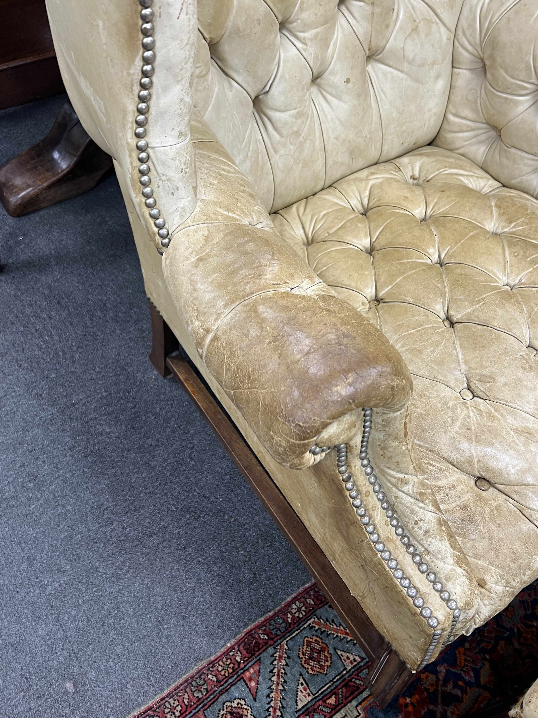 A George III style mahogany and buttoned leather wing armchair, width 80cm, depth 75cm, height 110cm with footstool